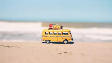 Pequeña furgoneta amarilla en la playa con equipaje en el techo.